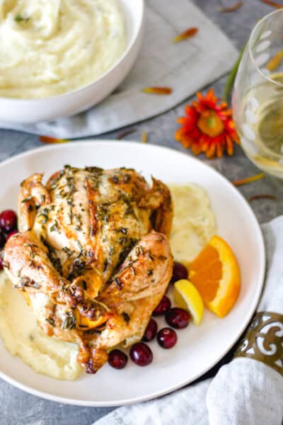 An Herb-Crusted Cornish Game Hen, on a plate with parsnip purée, surrounded by fresh flowers and a glass of white wine.