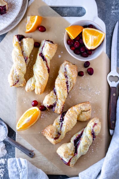 Baked Cranberry-Orange Twists drizzled with orange icing and sitting on a marble board.