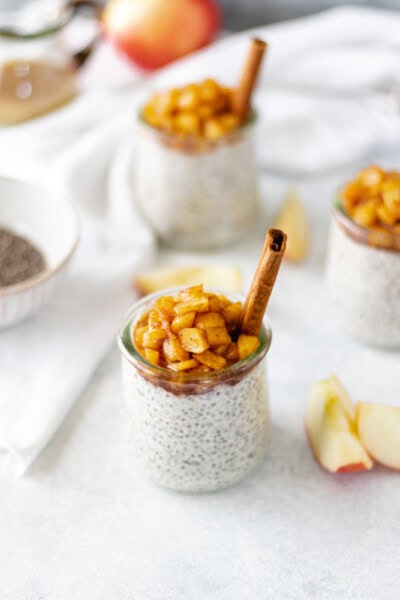Apple Pie Chia Pudding in small jars topped with cooked apples and a cinnamon stick.