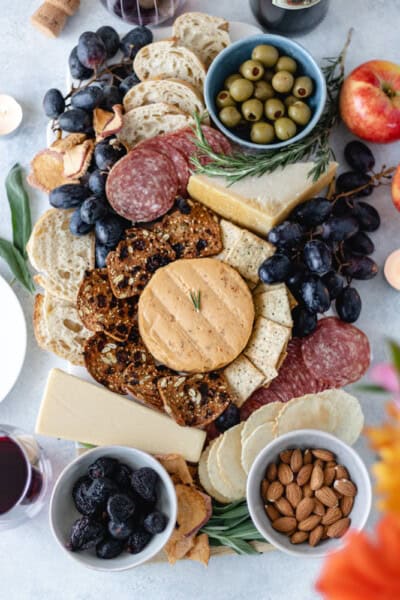 A marble board topped with meat, cheeses (dairy and dairy-free), fruits and crackers surrounded by wine and fresh flowers.