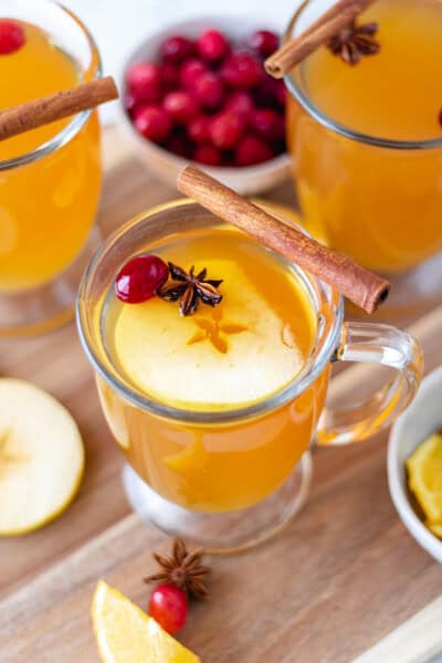 Three glasses of Mulled Apple Cider on a circular wood cutting board.