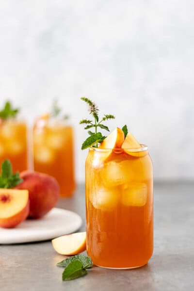 A glass filled with peach lavender iced tea, fresh peach slices and mint.
