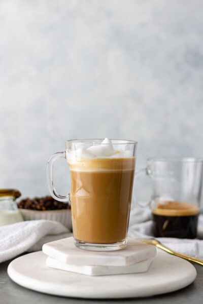 A hot Homemade Vanilla Bean Latte, in a glass mug, sitting on a stack of marble coasters.