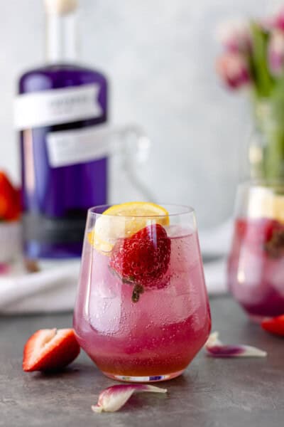 Strawberry Lavender Gin & Tonic in a glass and topped with a fresh strawberry and lemon wedge.