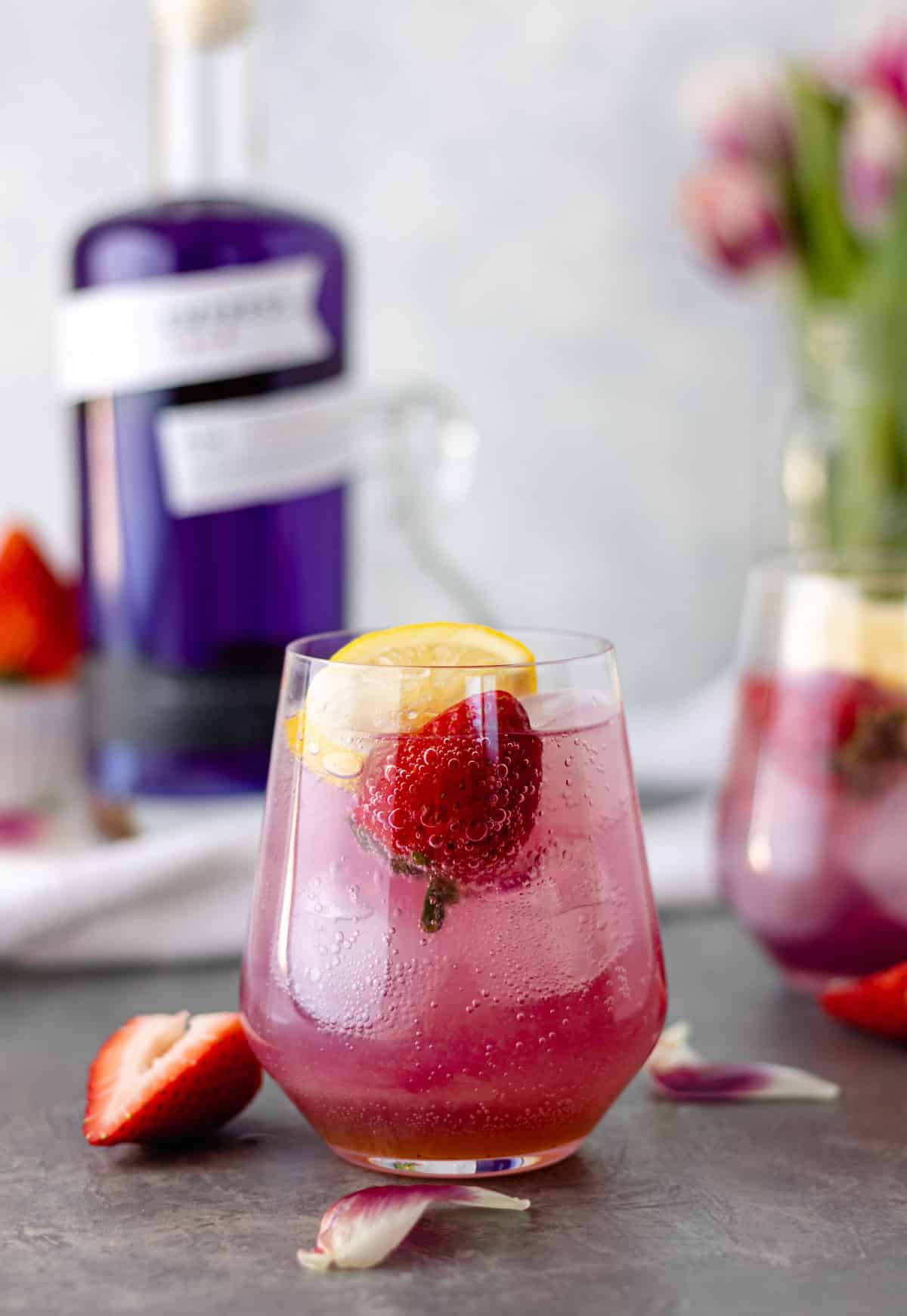 Strawberry Lavender Gin & Tonic in a glass and topped with a fresh strawberry and lemon wedge.