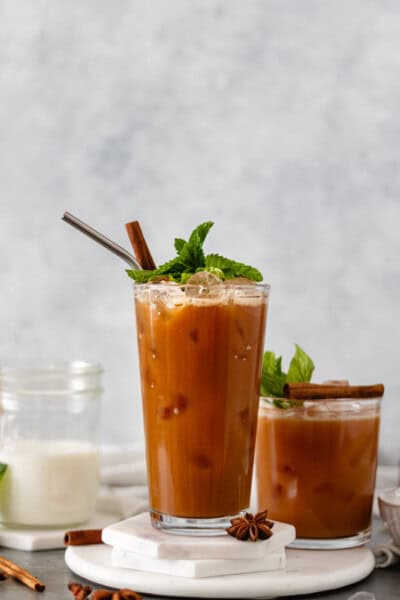 Sweet-Coconut Thai Chai Iced Tea in two glasses and topped with fresh mint and a cinnamon stick.