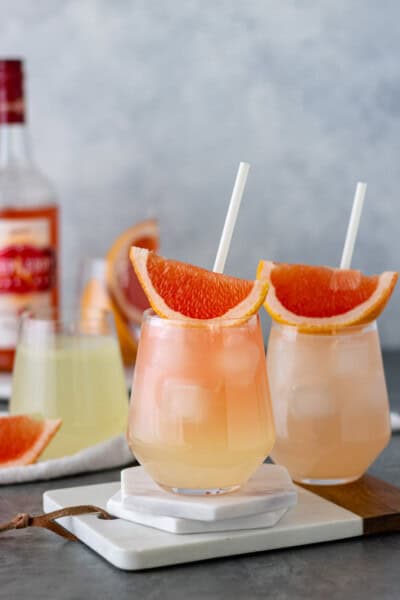 Two glasses of Grapefruit Vodka Lemonade topped with grapefruit wedges, and surrounded by lemonade, grapefruit and vodka.