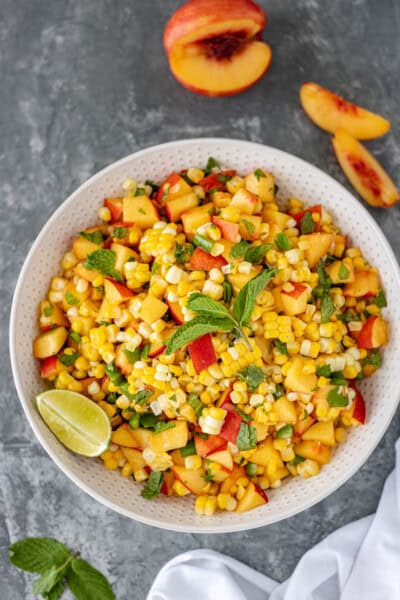 Fresh Nectarine Corn Salsa in a large serving bowl and surrounded by nectarine slices, fresh mint and a white towel.