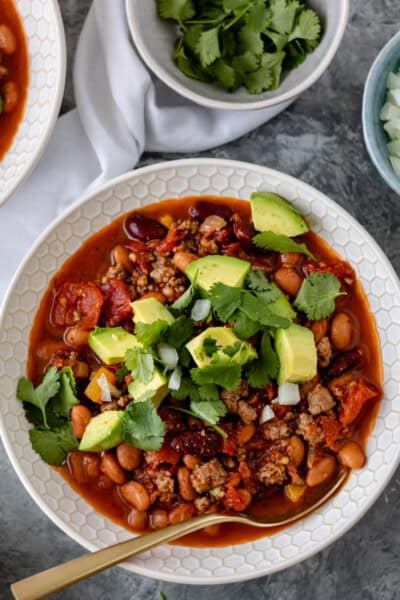 Two bowls of Chicken Chipotle Chili topped with avocado chunks, diced onion and fresh cilantro.