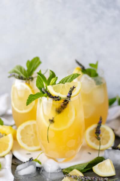 Boozy Mint-Lavender Lemonade Punch, in three stemless glasses, sitting on a marble trivet and topped with fresh mint, fresh lavender sprigs and lemon slices.