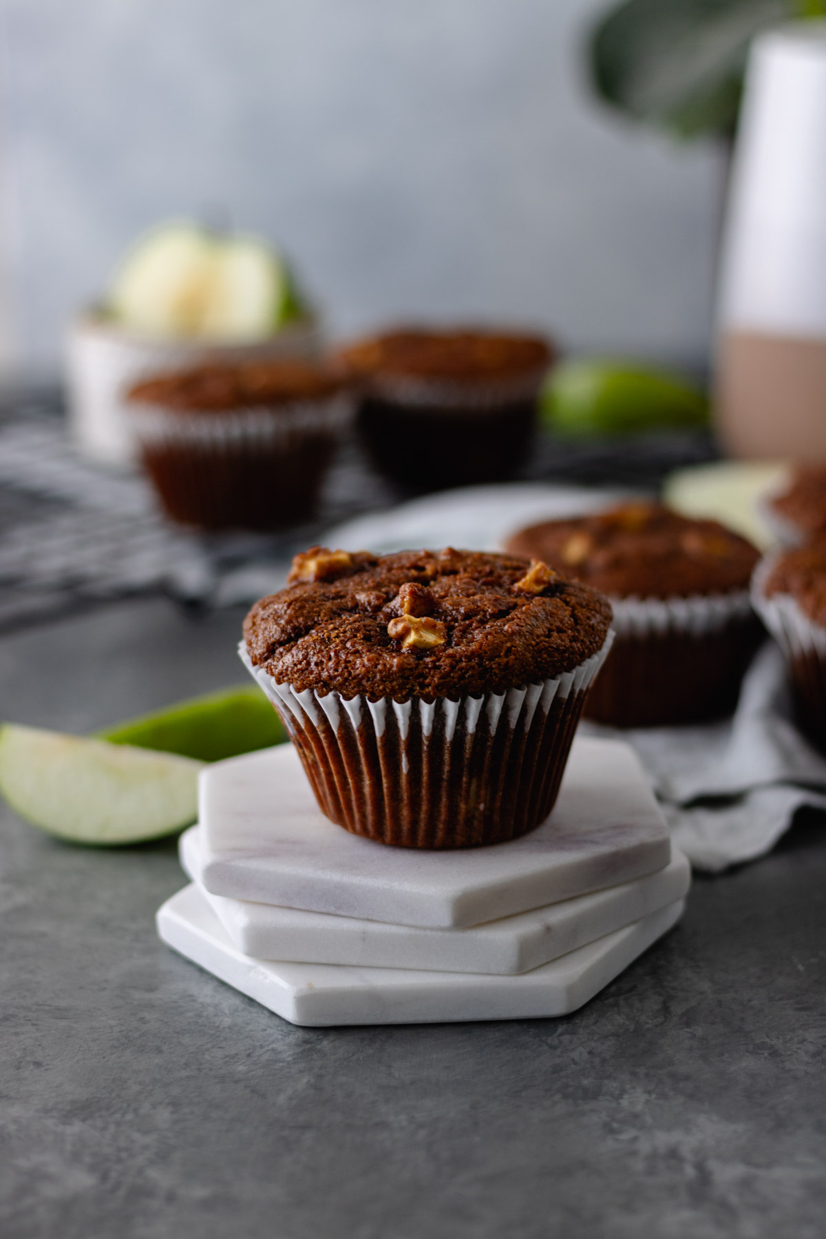A baked Apple-Cinnamon-Zucchini Muffin topped with cinnamon sugar and surrounded by Granny Smith apple slices and more muffins.