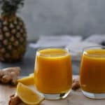 Two glasses of Immune Boosting Wellness Shots, topped with black pepper, and sitting on a rectangular marble bread board.