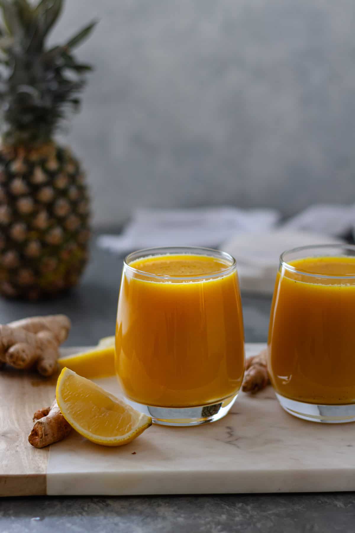 Two glasses of Immune Boosting Wellness Shots, topped with black pepper, and sitting on a rectangular marble bread board.