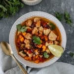 Spicy-Sweet Potato Bean Soup with Chicken in a glass bowl and topped with fresh cilantro and a lime wedge.