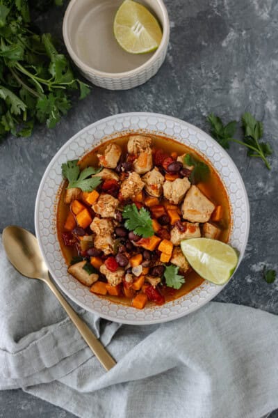 Spicy-Sweet Potato Bean Soup with Chicken in a glass bowl and topped with fresh cilantro and a lime wedge.