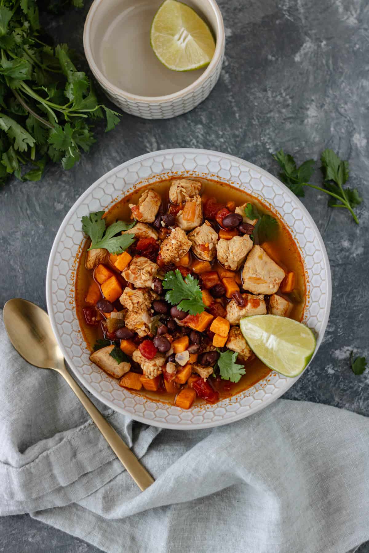 Spicy-Sweet Potato Bean Soup with Chicken in a glass bowl and topped with fresh cilantro and a lime wedge.